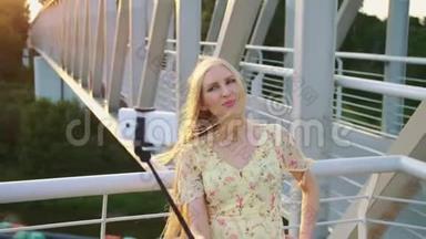 女人在桥上<strong>自拍</strong>。 站在人行桥上的一位开朗漂亮的金发女郎和monopod<strong>一起自拍</strong>